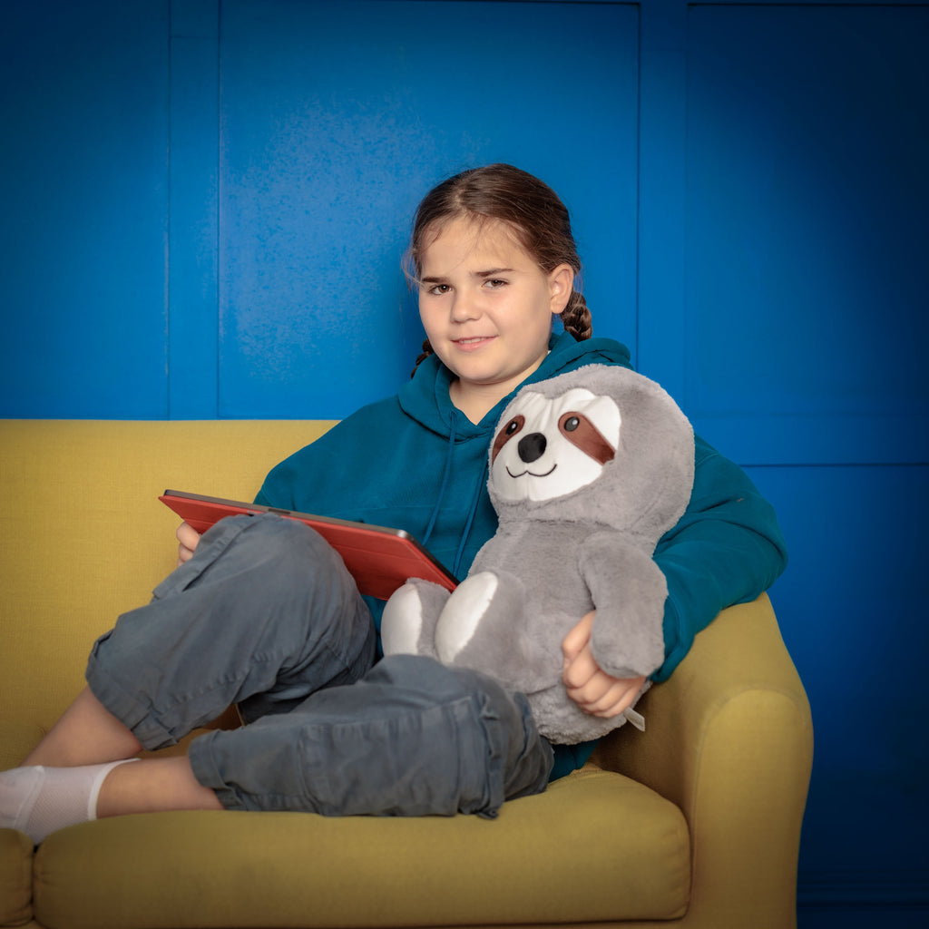 Girl using a tablet on a couch, with Tranquil Sloth beside her providing emotional support.