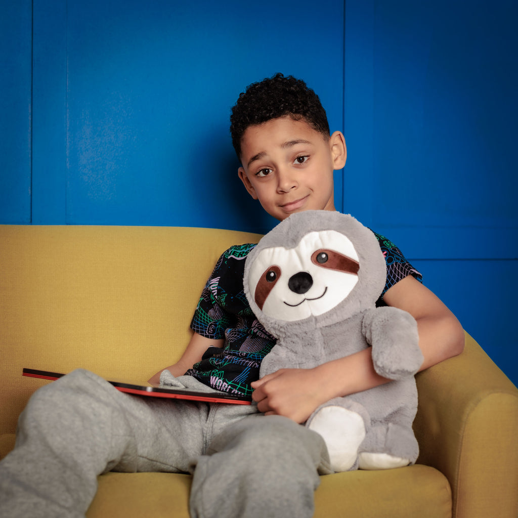 Boy sitting on a couch holding Tranquil Sloth and a tablet, engaged in an educational app.