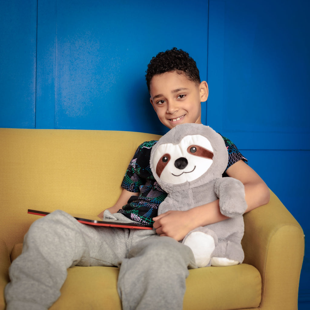 Boy sitting on a couch holding Tranquil Sloth and a tablet, engaged in an educational app.