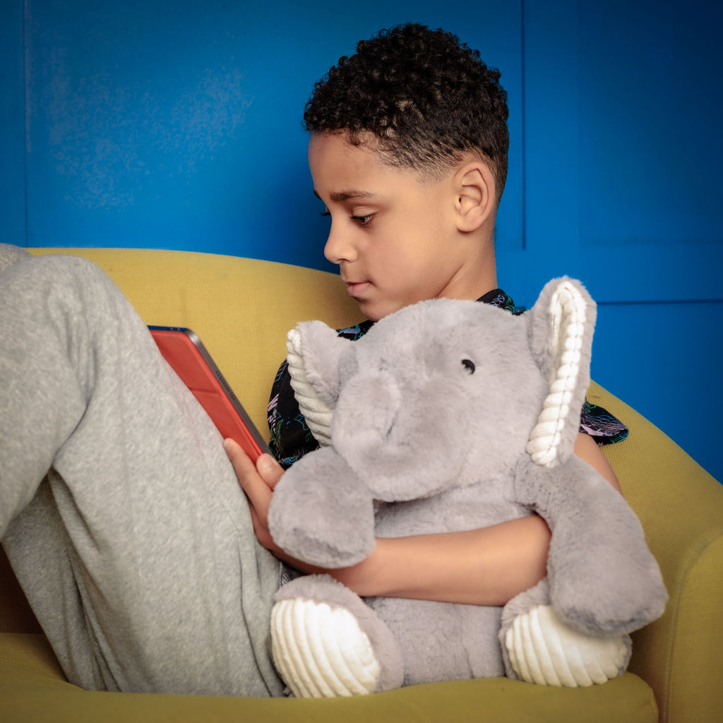 Boy sitting on a couch with Empowerment Elephant and a tablet, looking inspired by an educational game.