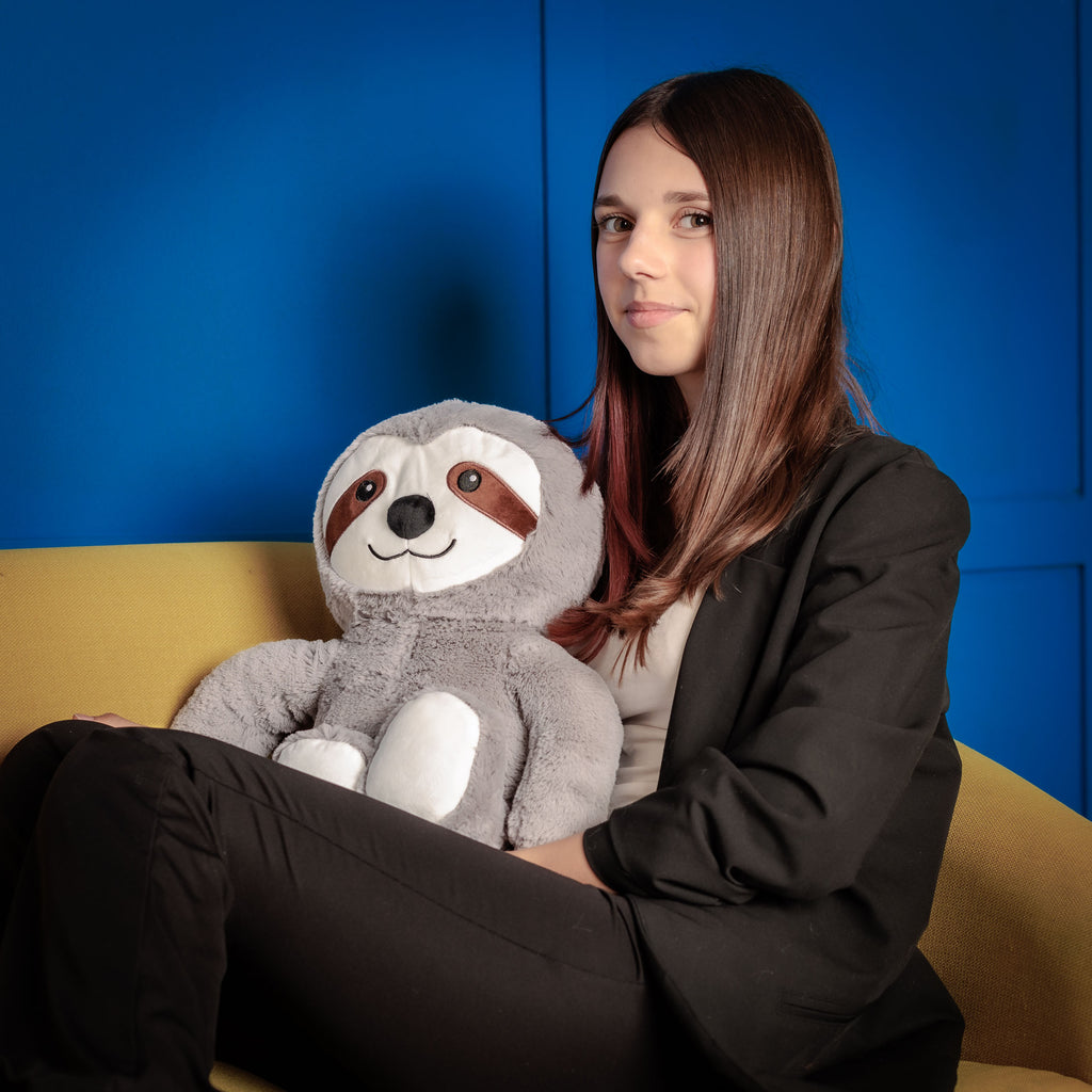 Girl on a couch cuddling with Tranquil Sloth.