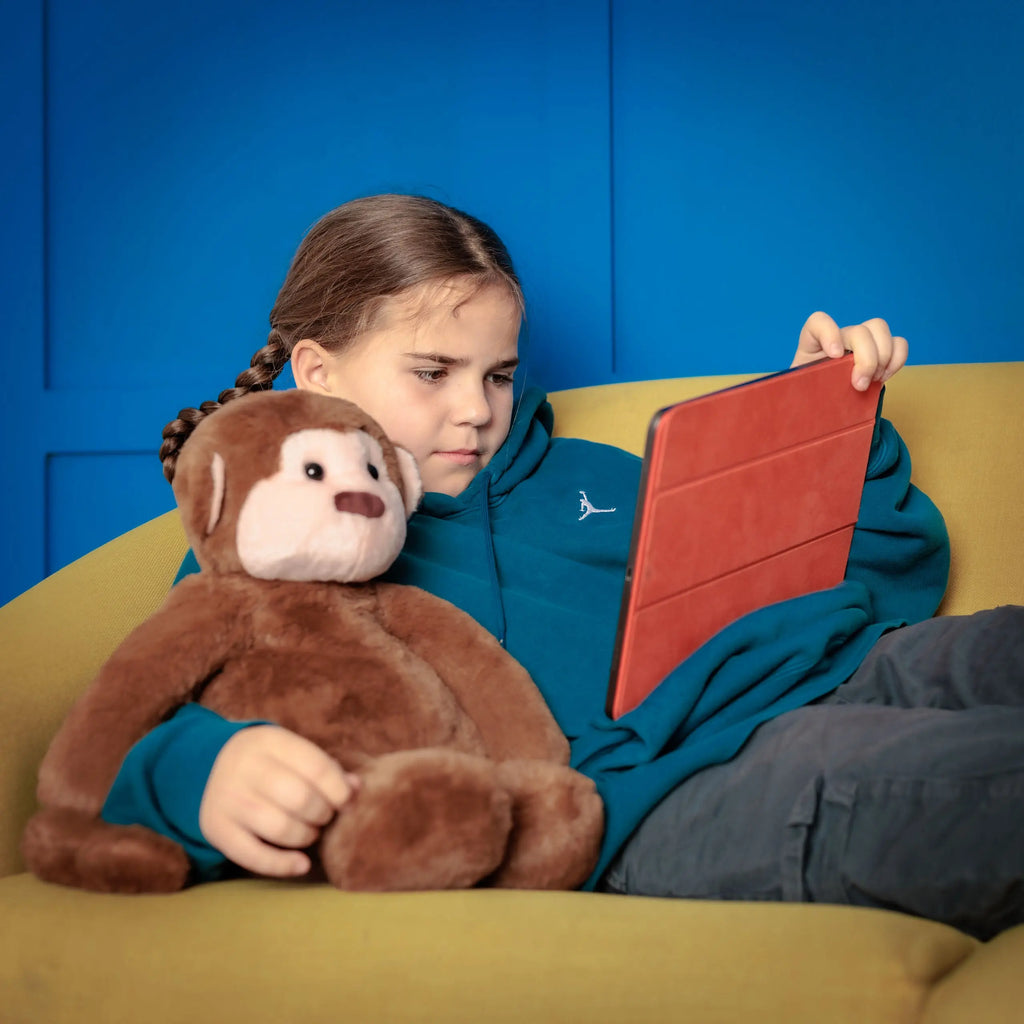 Girl holding Motivational Monkey while sitting on a couch and interacting with a tablet.