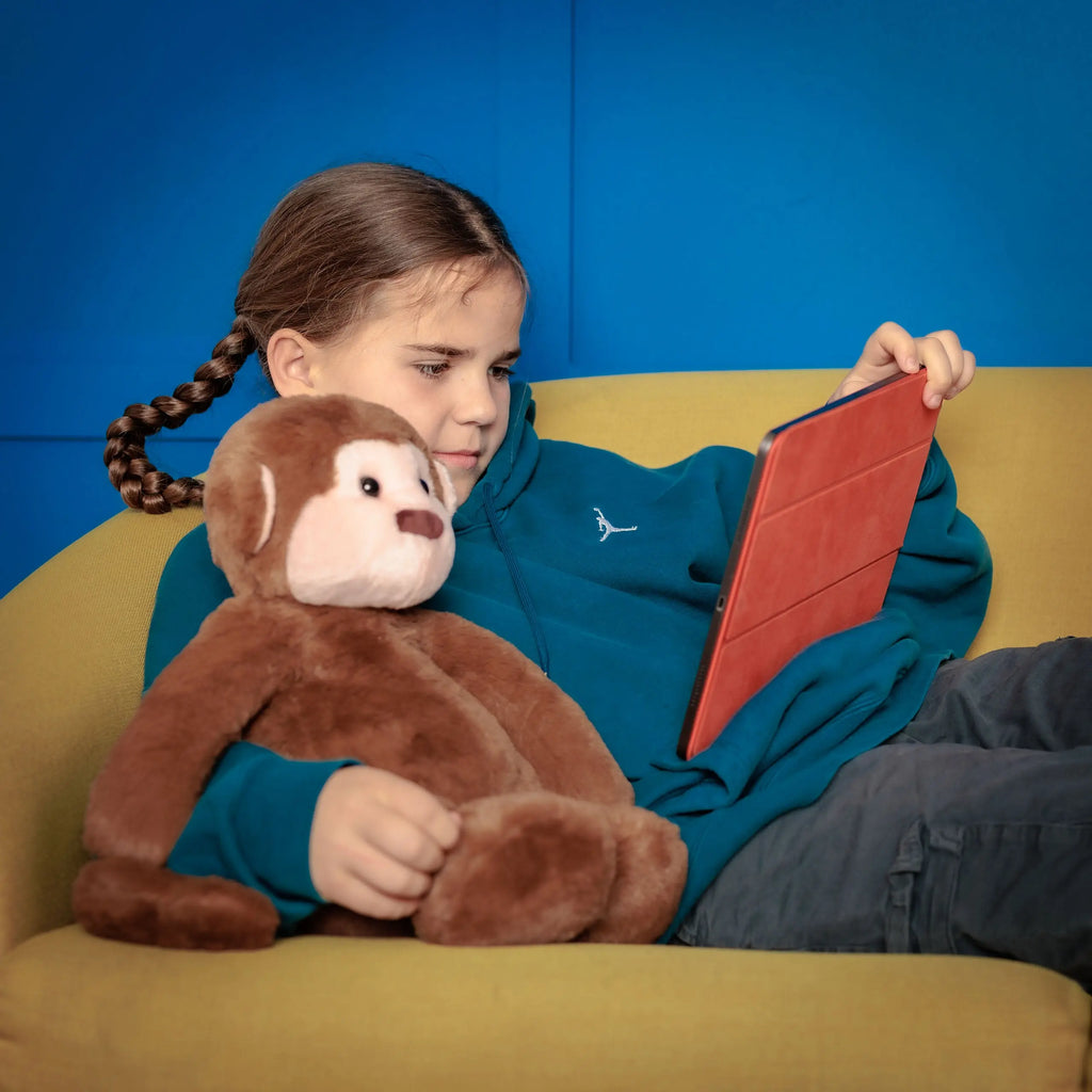 Girl holding Motivational Monkey while sitting on a couch and interacting with a tablet.