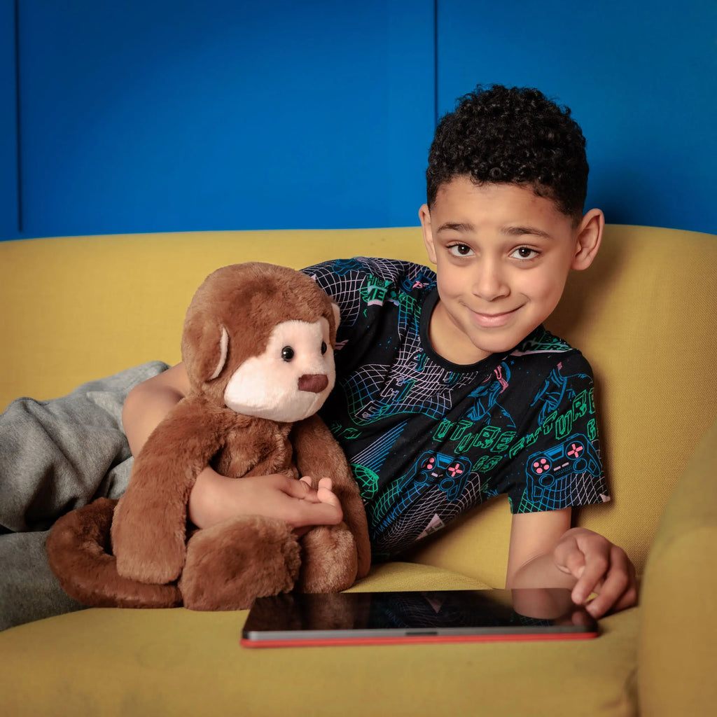 Boy smiling with Motivational Monkey on a couch, both engaging with educational content on a tablet.