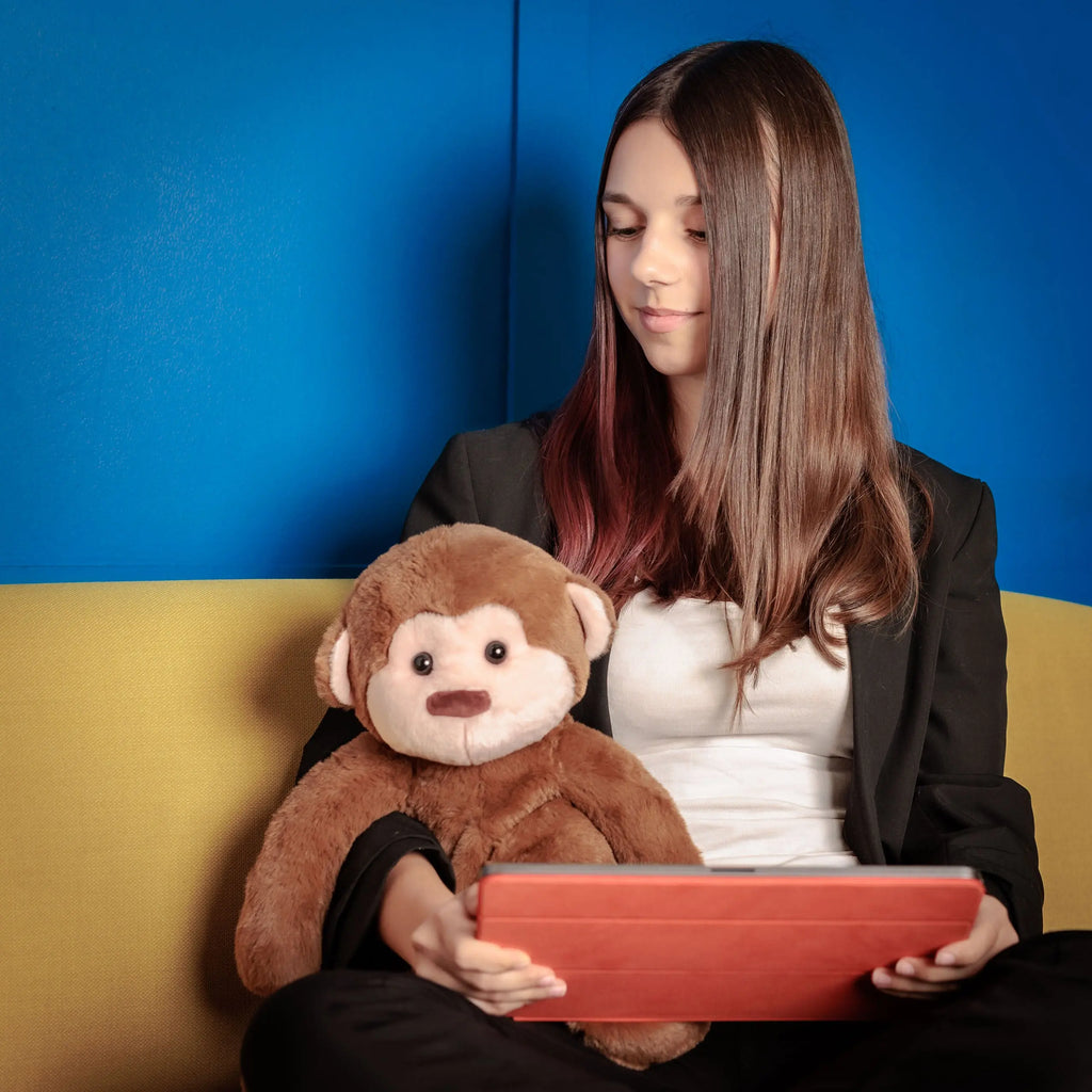 Girl and Motivational Monkey on a couch, the toy sitting upright as she uses a learning app on a tablet.